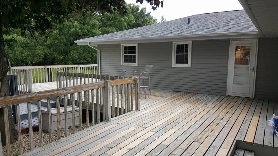 Weathered wooden deck and railings off the back of a gray-sided house, before work