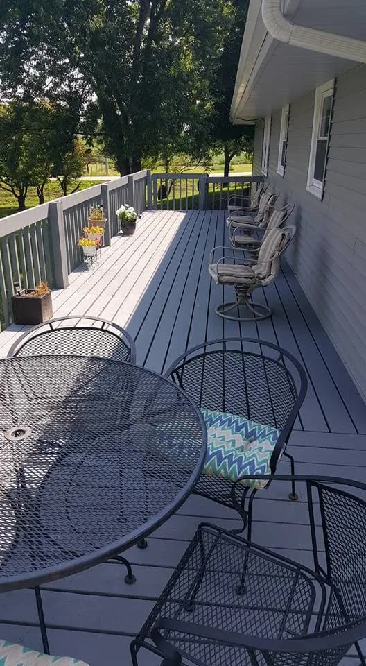The same deck after painting, boards and railings an even gray, with patio furniture set out