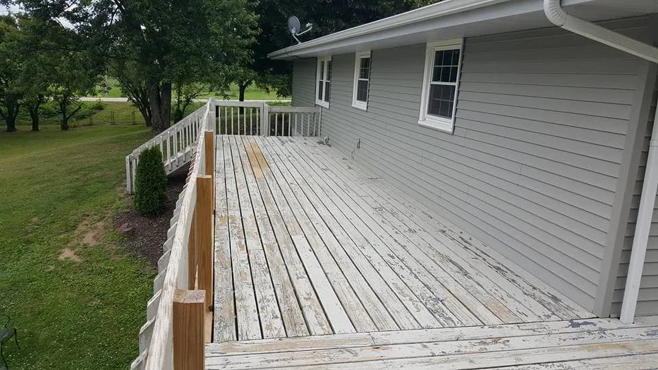 Long wooden deck along gray siding, with worn, peeling gray-white boards and railings