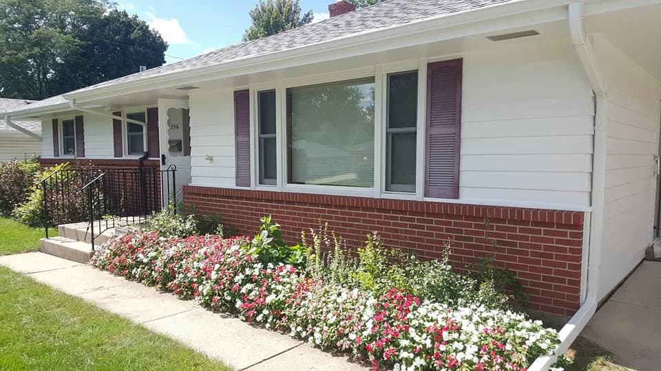Brick and white-sided ranch house with burgundy shutters and a flower bed out front