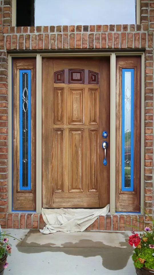 Wood front door with sidelights, faded and blotchy, taped off and on drop cloths mid-job